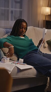 Vertical shot of young African American woman lying on sofa, looking stressed while reviewing past due bills and checking smartphone. Clip is perfect for debt relief or financial planning ads