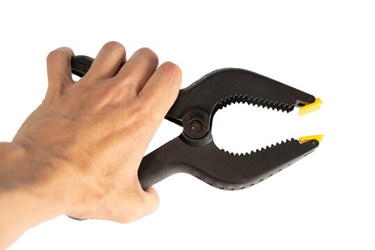 Hand holding a black clamp tool with yellow tips in a bright setting