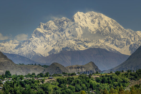 View of the snow-capped trich mir peak of the Hindu Kush mountain range rising above a lush green valley with small village settlements in Chitral, Khyber Pakhtunkhwa, Pakistan.