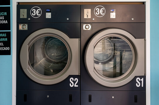 Two large front load dryers labeled S1 and S2 in a modern self service laundromat with blue tiled walls in Spain a clean and convenient coin operated launderette for everyday laundry chores.