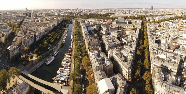Aerial view of Canal Saint-Martin with boats moored along the banks, surrounded by dense urban architecture and tree-lined streets in Paris, Ile-de-France, France.