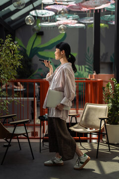 Woman walking through cafe speaking on phone holding laptop