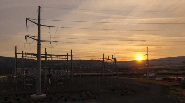 Aerial view of The Dalles data center power substation with electrical towers and transmission lines silhouetted against a golden sunset sky in The Dalles, Oregon, United States.