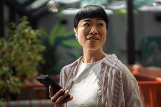 Asian woman connecting with smartphone in urban garden