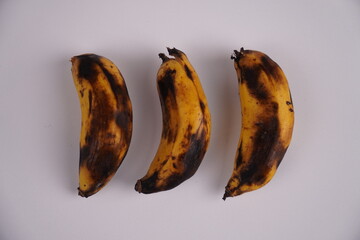 A close-up, top view showing three bananas on a plain white surface. Their yellow skins display brown and black spots, as well as signs of ripeness. © Ari Triyanto