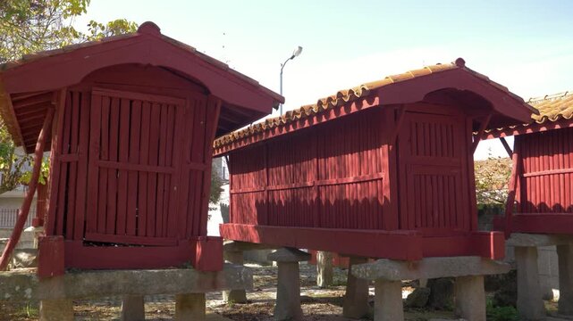 Traditional red horreos rise on stone supports in A Forxa, Porqueira, Galicia, Spain