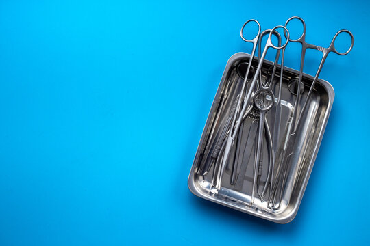Sterile surgical instruments and tools - scalpels, scissors and others - in a stainless tray on blue background, top view