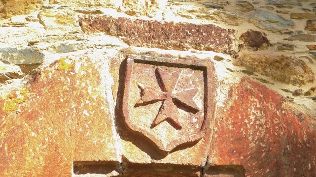 Close-up of a carved heraldic stone detail on San Miguel de Xagoaza, revealing an aged coat of arms embedded in the historic masonry of the church complex in Galicia