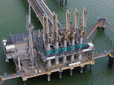 Aerial view of an industrial marine loading terminal featuring multiple loading arms and pipelines on a steel platform extending over the water in the United Kingdom.