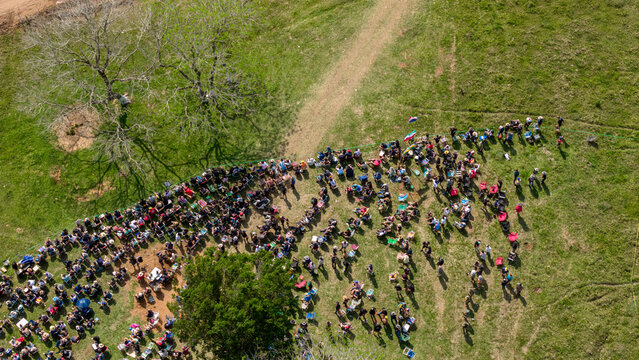 Aerial view of Rally Paraguay with a large crowd of spectators gathered along a dirt track in a grassy field in Nueva Alborada, Itapua Department, Paraguay.