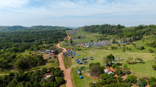 Aerial view of the Rally Paraguay event featuring numerous spectator tents and vehicles scattered across a green field alongside a winding dirt road in Nueva Alborada, Itapua Department, Paraguay.