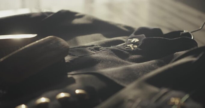 Pan shot reveals soft sunlight falling across a traditional miner's ceremonial dress uniform laid out for careful brush cleaning and garment maintenance.