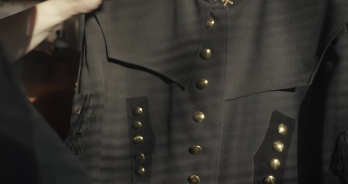 Garment caretaker brushes a traditional miner's Bergmannstracht ceremonial tunic, featuring rows of buttons and crossed hammer and mallet insignia.