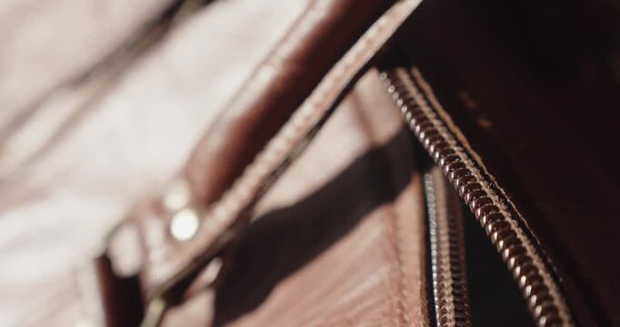 Macro detail shows an old worn leather travel bag being zipped open in ambient sunlight, creating a nostalgic journey background.
