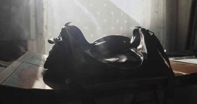 Person places an old leather travel bag on a road map beside a brightly lit window, creating a nostalgic travel B-roll scene.