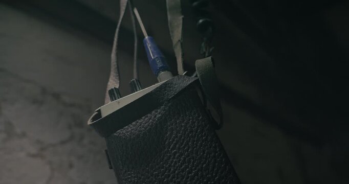 Low angle reveals a retro walkie talkie hanging inside a low lit wartime command bunker with flashing cinematic illumination.