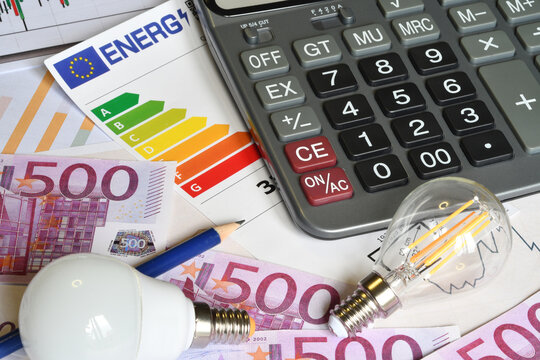 Energy efficiency class label with calculator, euro banknotes and light bulbs on desk, electricity bill and utility cost concept