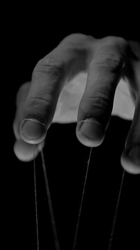 Vertical video. Monochrome Puppeteer Hand Controls Hanging Strings in Darkness, Symbolizing Political Influence, Authority and Manipulation of Society