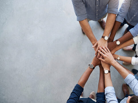 A diverse group of business people stacking their hands together in a circle, symbolizing teamwork and unity from an overhead perspective.