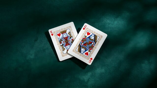 Two playing cards, king and queen, on dark green table with shadows, close-up