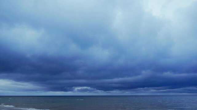 Static seascape panorama displays heavy dark rain clouds hanging low over open waters of Baltic Sea during dramatic summer weather change at Jurmala coast.
