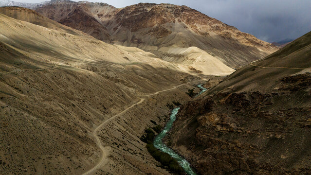 Aerial view of the Panj River winding through the rugged, arid mountains of the Wakhan Valley, with a dirt road following the riverbank in Wakhan, Badakhshan, Afghanistan.
