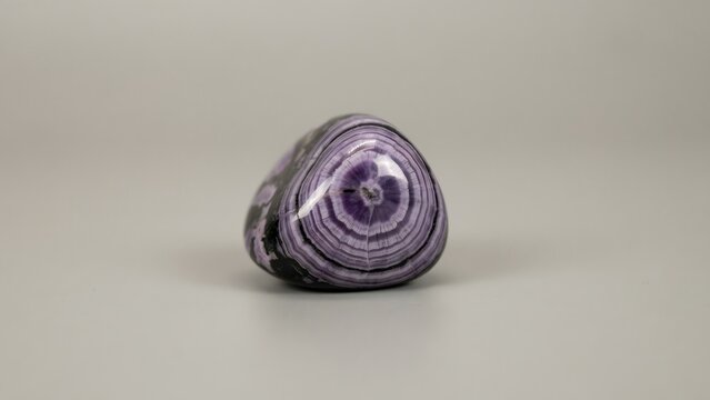 Polished purple and white banded geometric gemstone on plain surface