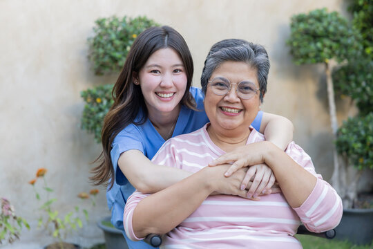 Smiling woman hugs older woman in garden during sunny day