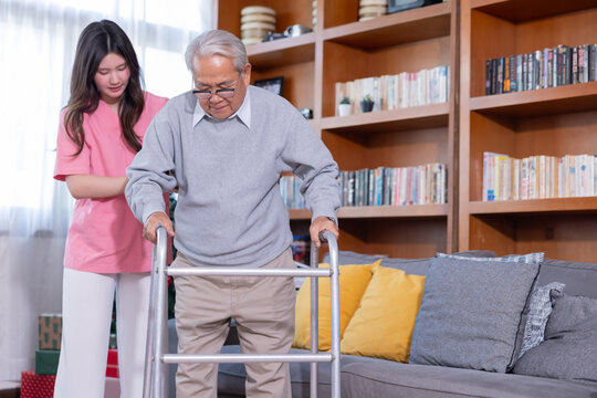 A young woman assists an elderly woman using a walker in a room