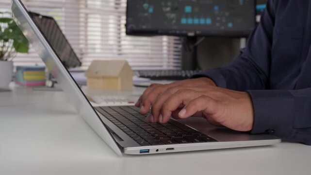 Businessman hands typing on laptop keyboard with house model on office desk, concept of real estate investment, property mortgage planning, housing loan application, and digital business.