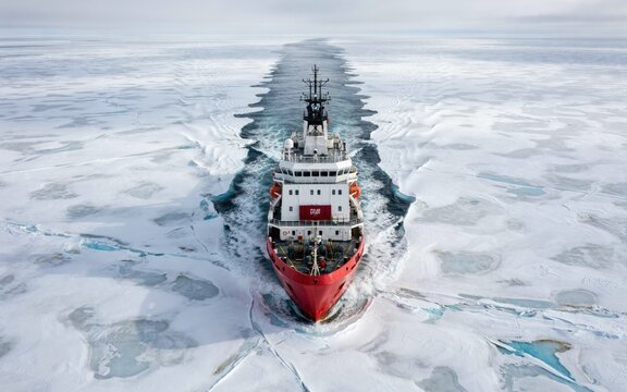 Aerial view of a red icebreaker ship cutting through arctic sea ice