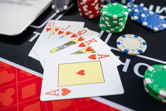 Top View of Royal Flush Hearts Hand with Casino Tokens and Laptop for Virtual Poker Game