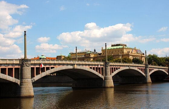 Prague, Czech Republic: Historic bridge over Vltava River with ornate architecture and city landmarks under blue summer sky.
