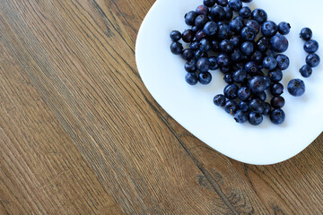 Blueberries and Ripe Berries Filled in White Porcelain Bowl Placed on Wooden Kitchen Desk © yaviki