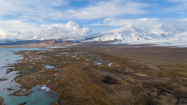 Aerial view of Karakul Lake surrounded by snow-capped mountains and vast arid plains under a blue sky in Chah Ab, Gorno-Badakhshan Auto, Tajikistan.
