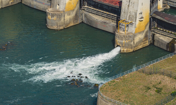 Aerial view of water discharging from a river dam sluice gate, showing hydraulic engineering and controlled river flow infrastructure in Le Pouzin, Auvergne-Rhone-Alpes, France.