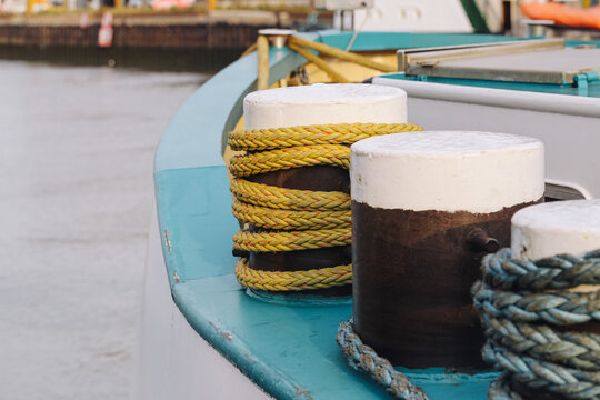 Heavy mooring bollards wrapped with thick yellow and blue ropes on boat deck. Nautical equipment near calm water forms maritime transport detail with harbor vessel and marine background.