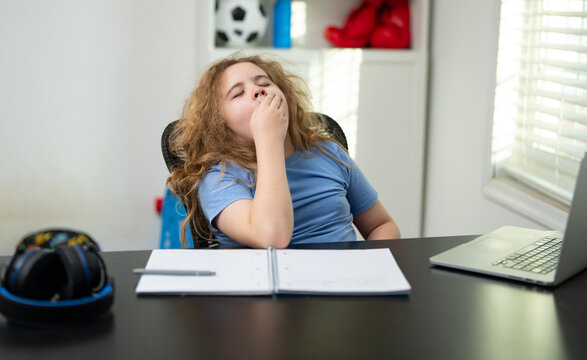 Sleepy kid at the school desk bored. Tired student needing a break from learning bored. Kid yawning while sitting at the laptop bored. Tired child study fatigue bored.