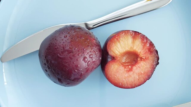 Ripe, juicy plums with fork and knife on a blue plate. Juicy plum cut in a half. Fruits and time of harvesting. Juicy plums sprinkled with water close up.