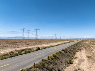 Naklejka premium high voltage power transmission towers alongside a desert highway under blue sky