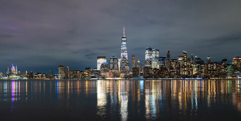 Naklejka premium New York Manhattan skyline illuminated. New York riverfront towers reflected. New York evening waterfront panorama. New York famous cityscape.