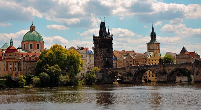 Prague, Czech Republic: Charles Bridge over Vltava River with Old Town Bridge Tower and historic Prague skyline under cloudy summer sky.