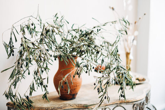 Close-up of Olive Branches in a rustic vase next to a candle on a sideboard 