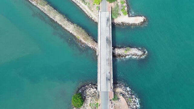 An aerial drone view of the coastal road in Ulee Lheue, Banda Aceh, leading towards the ferry port to Sabang Island, surrounded by calm sea waters and mountains.
