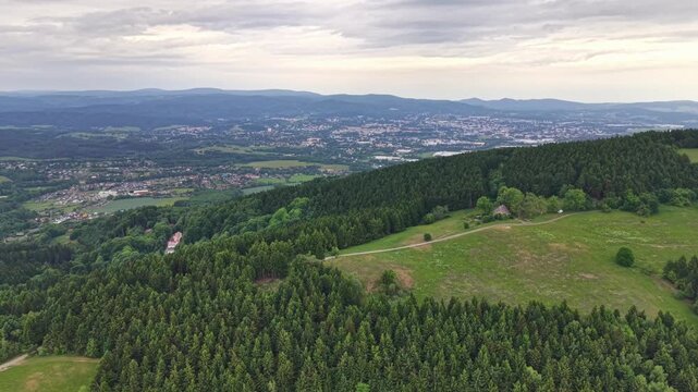 Panoramic landscape static view, in open countryside with hills and distant cityscape, with green fields, trees, hills, city buildings, from a aerial perspective, with green, brown accents.