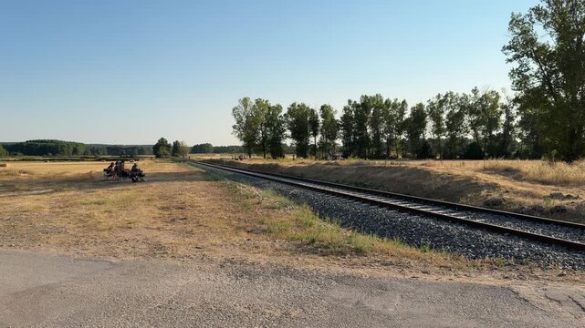 Idyllic summer landscape featuring empty railway tracks curving through a dry, grassy field under a clear blue sky on a warm, sunny day