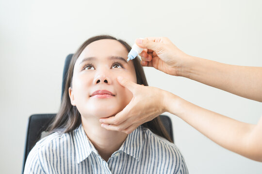 Asian young woman receiving medical eye drops from a doctor or optometrist to treat dry eye syndrome and redness irritation during an ophthalmology examination in health clinic, isolated on background