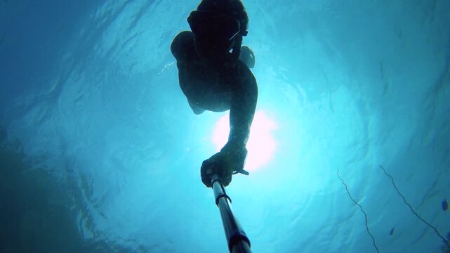 selfie of an asian female woman wearing snorkel mask fin free diving down into the deep water depth from bottom to top view in dark atmosphere look up to diver silhouette surface underwater in ocean s