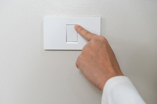 Asian young woman hand turn off on lighting switch at home room. Finger pushing light switch turn on or off white switch on wall for saving, control power electrical energy, eco environment concept.