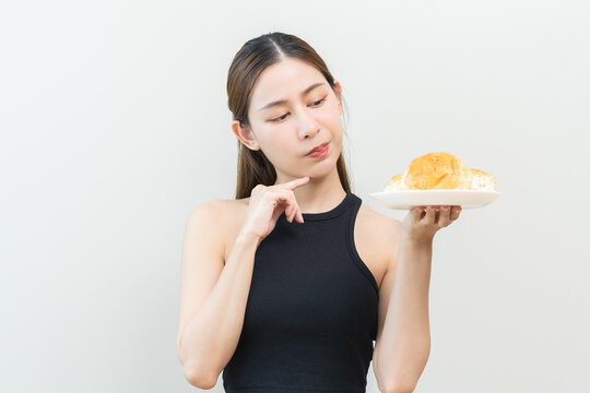 Gluten allergy concept with a young beautiful Asian woman holding a plate of fresh bread bakery and thinking or refusing to eat on an isolated white background for health and diet themes.